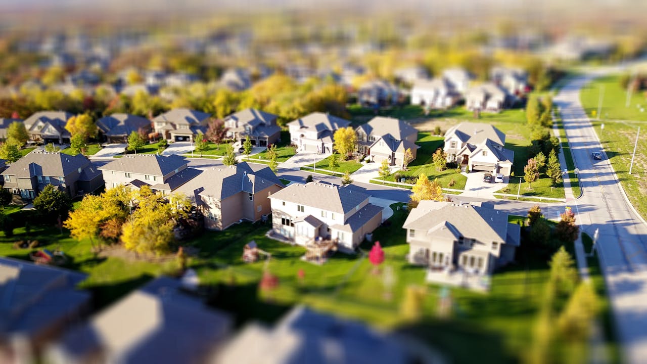 about-us Tilt-shift aerial photo of a suburban neighborhood with green lawns and roads.